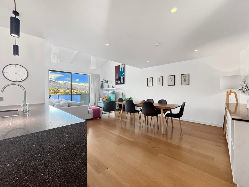 A modern kitchen with a granite countertop, a dining area with a wooden table and chairs, and a large window with a mountain view.