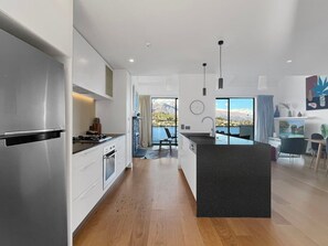 A modern kitchen with a central island, wooden flooring, and a view of mountains through large windows.