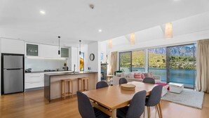 A modern kitchen with a central island, a dining area with a wooden table and chairs, and a large window offering a scenic mountain view.