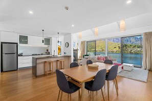 A modern kitchen with a central island, a dining area with a wooden table and chairs, and a large window offering a scenic mountain view.