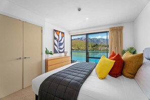 A bedroom with a bed, a dresser, a window with a mountain view, and a painting on the wall.