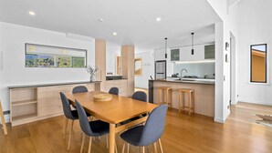 A modern kitchen with a dining area, wooden flooring, and a large window with a view of the countryside.