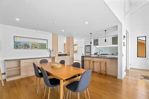 A modern kitchen with a dining area, wooden flooring, and a large window with a view of the countryside.
