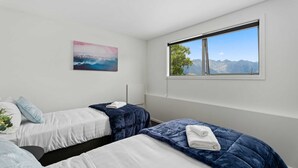 Une chambre d’hôtel avec deux lits, une grande fenêtre donnant sur les montagnes et un tableau accroché au mur.
