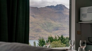 Une pièce avec vue sur un paysage montagneux, visible à travers une fenêtre, une table à manger avec des verres à vin, et un thermostat fixé au mur.