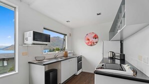 Une cuisine moderne équipée d’un four à micro-ondes, d’un évier et d’une cuisinière. Une fenêtre offre une vue sur les montagnes, et un tableau rond décoratif orne le mur.