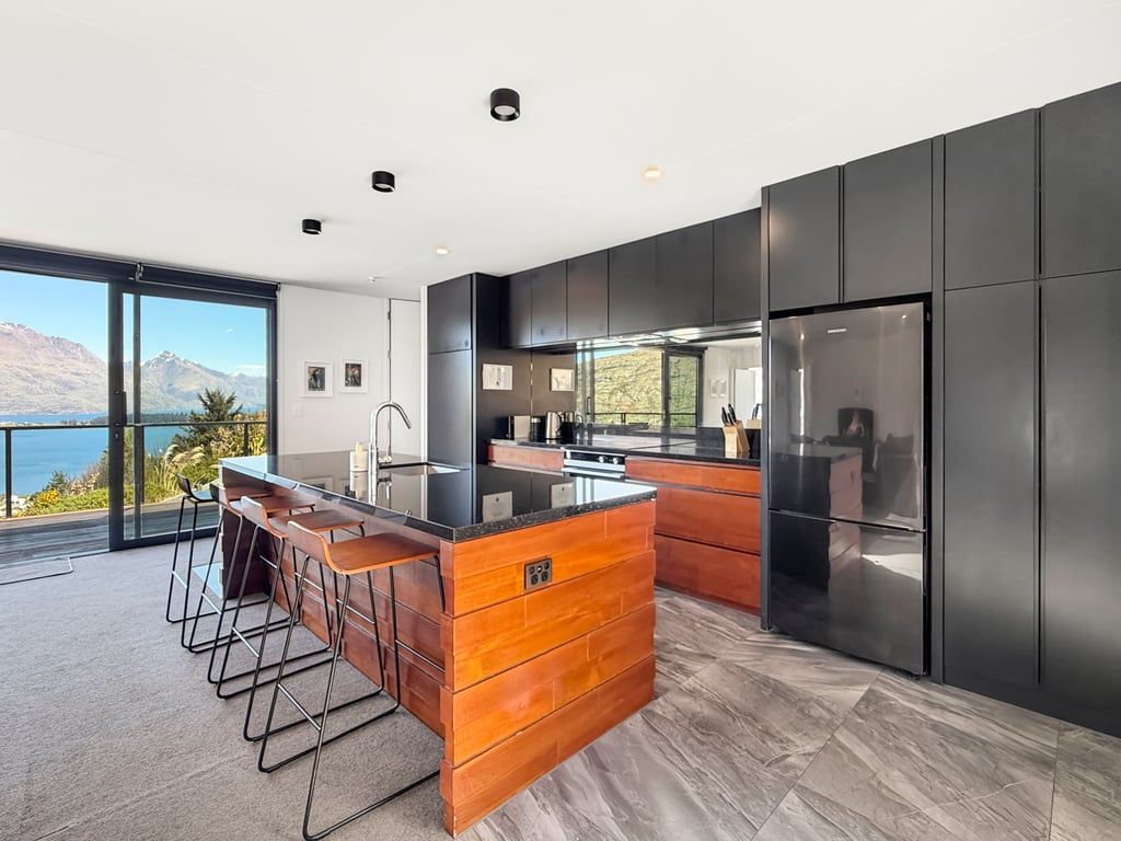 A modern kitchen with a central island, bar stools, and a large refrigerator.