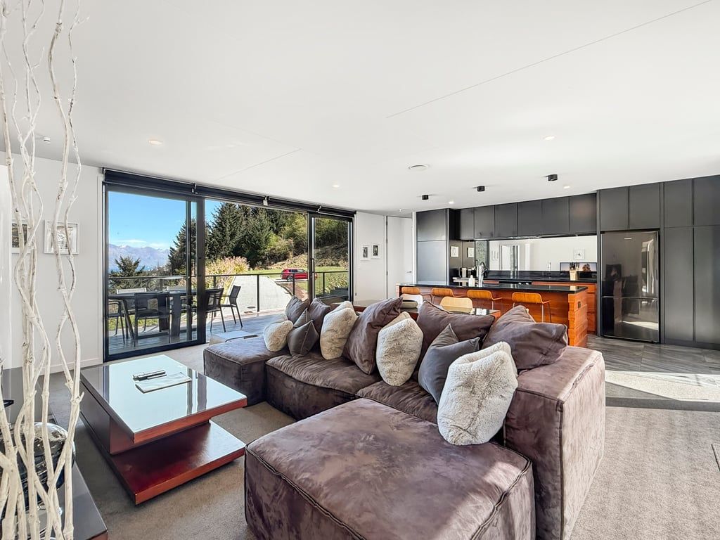A modern living room with a large sectional sofa, a glass dining table, and a kitchen in the background.