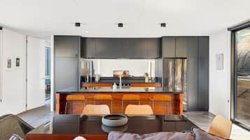 Une cuisine moderne avec des meubles de couleur sombre, un îlot central doté de tabourets, et un coin repas avec une table et des chaises.