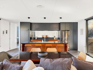 A modern kitchen with dark cabinetry, a central island with bar stools, and a dining area with a table and chairs.