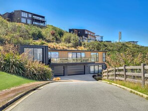 A modern house with a garage, a driveway, and a wooden fence. - Mountain Lake Vista 3 Bedroom (Queenstown)