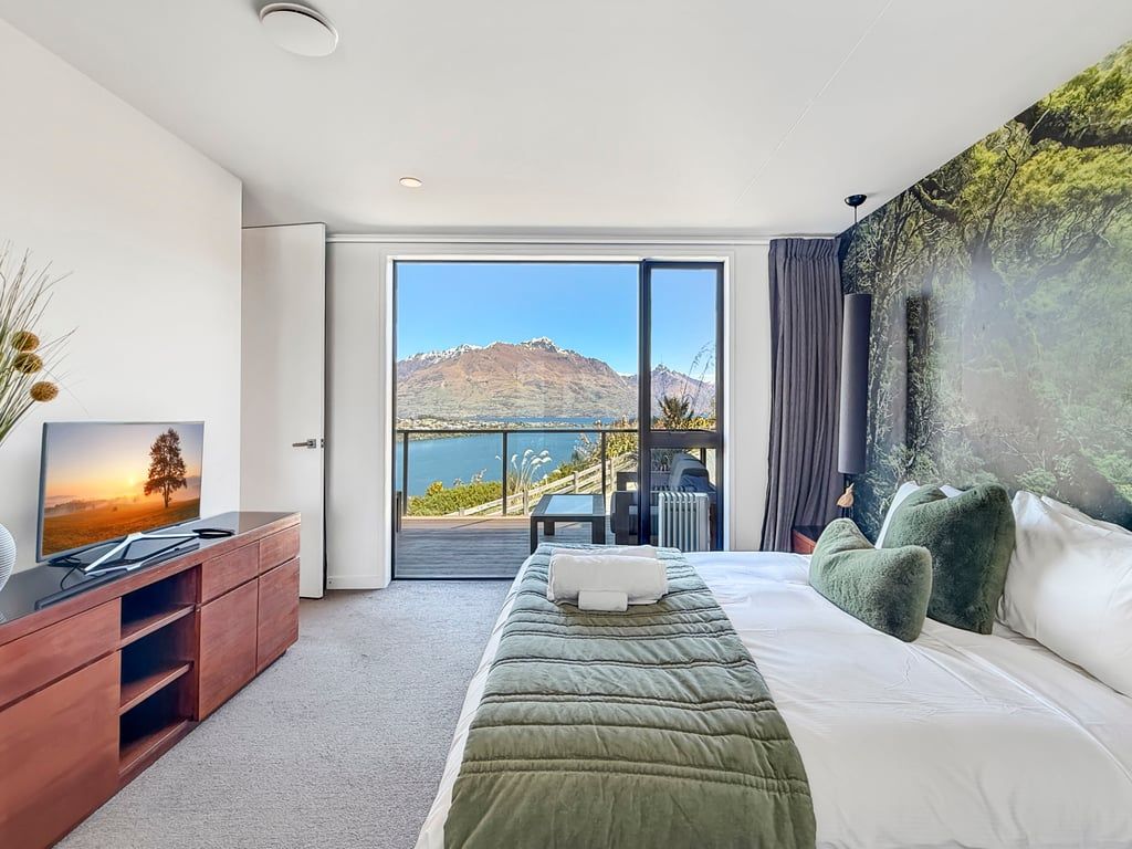 A bedroom with a large bed, a television, and a view of a mountain and lake through a sliding door.