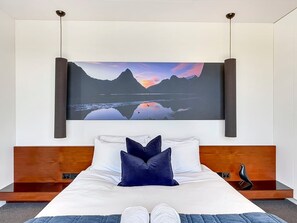 A bedroom with a bed, pillows, a bedside table, and a wall-mounted artwork. - Mountain Lake Vista 3 Bedroom (Queenstown)
