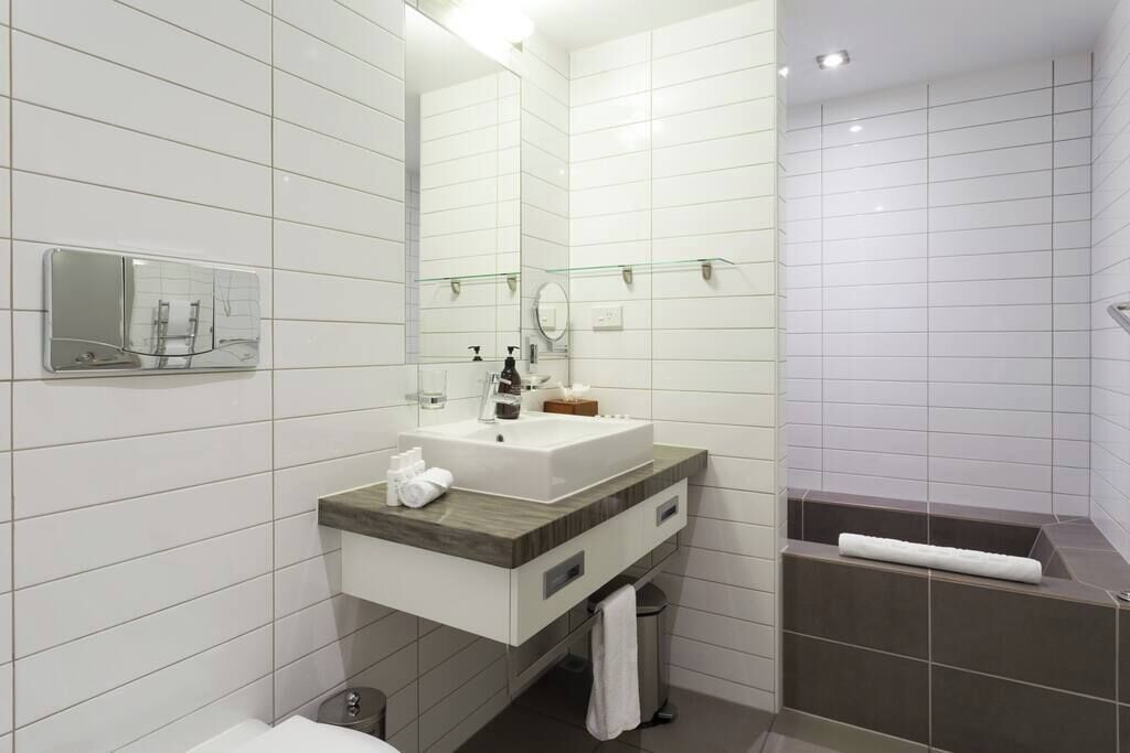 Un baño moderno con lavamanos, espejo y bañera blancos.