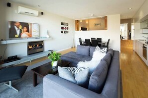 Un salon moderne avec un canapé gris, un téléviseur à écran plat, une cheminée et un coin repas comprenant une table et des chaises.