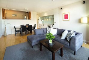 A modern living room with a grey sofa, a coffee table, and a dining area with a table and chairs.