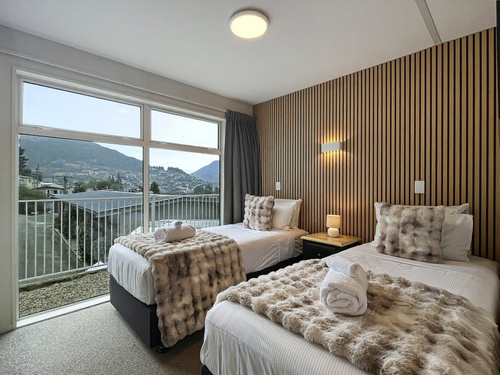 A hotel room with two beds, a balcony with a view, and a wooden wall panel.