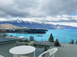A terrace with a table and chairs overlooking a lake with mountains in the background.