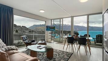 A modern living room with a glass table, leather sofa, and a view of mountains and a body of water.