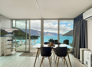 A modern room with a large sliding glass door leading to a balcony overlooking a lake and mountains.