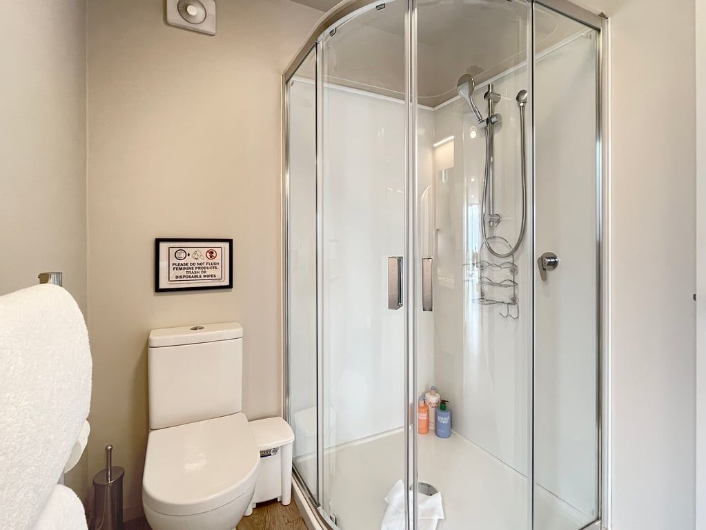 Een badkamer met een douche met glazen wand, een toilet en een bordje in een lijst aan de muur.