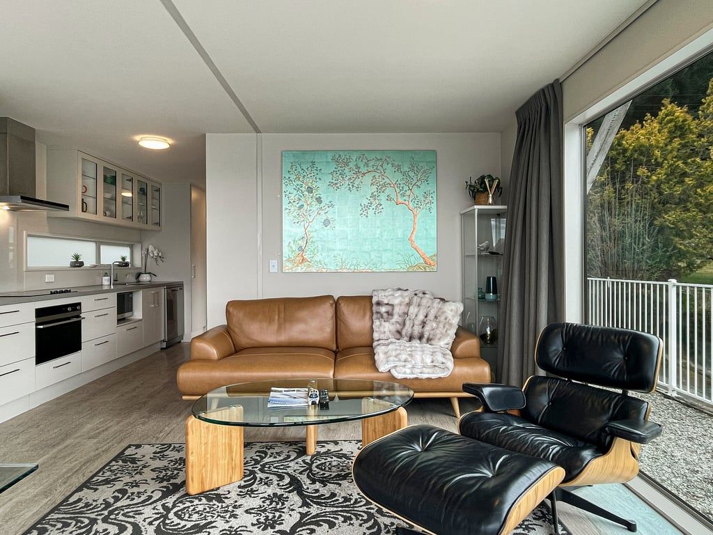 A modern living room with a sofa, a glass coffee table, and a black leather chair.