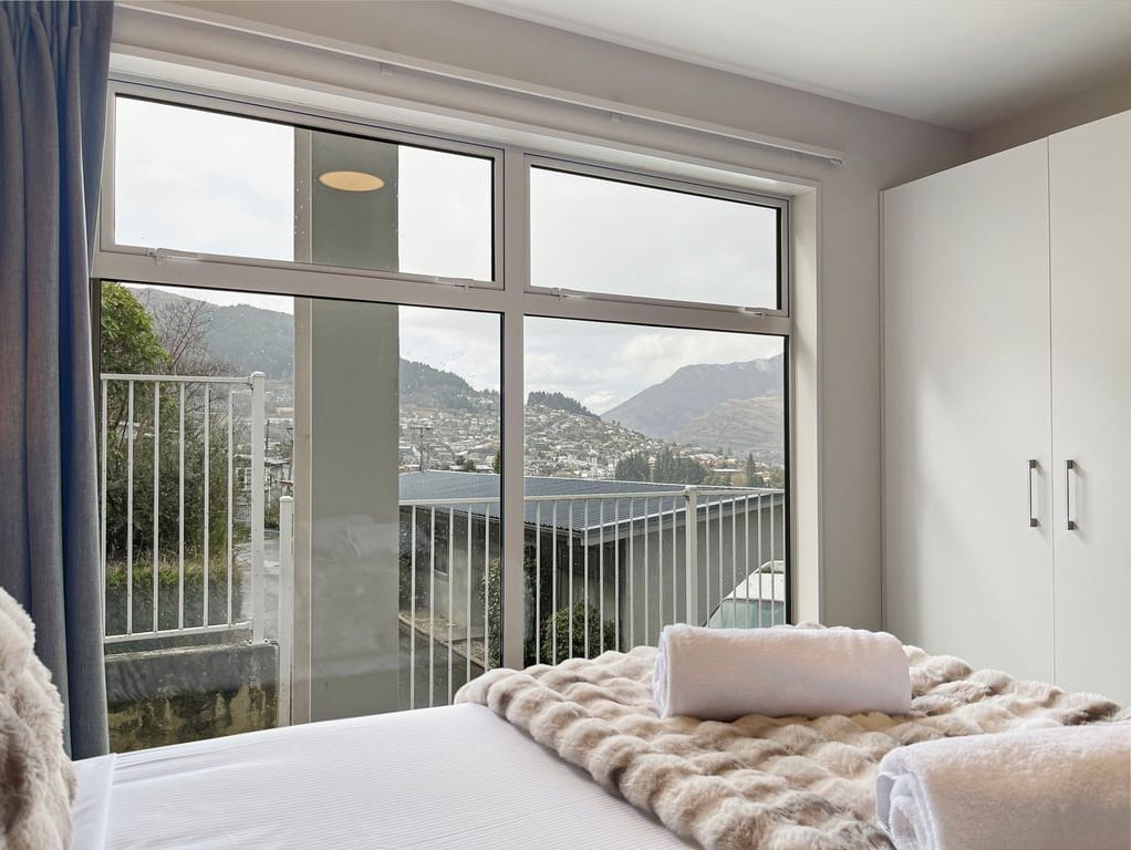 Ein Schlafzimmer mit großem Fenster, einem Bett mit weißer Decke und einem Kleiderschrank.