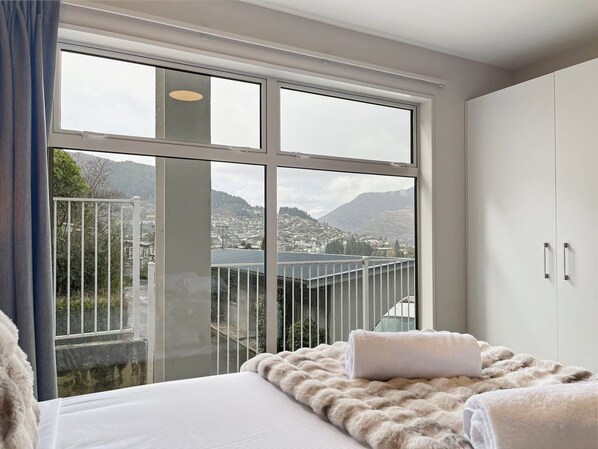 A bedroom with a large window, a bed with a white blanket, and a wardrobe.