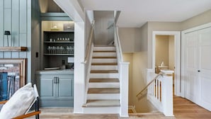 Eine Treppe führt zu einer zweiten Etage, ein Küchenbereich mit Schränken und Ablagefläche sowie ein Flur mit einer Tür.