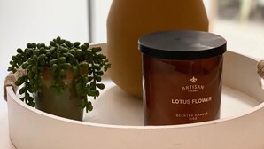 A round, white tray with a brown candle labeled "Lotus Flower" and a small potted plant. - Marina 303A-Studio (Queenstown)