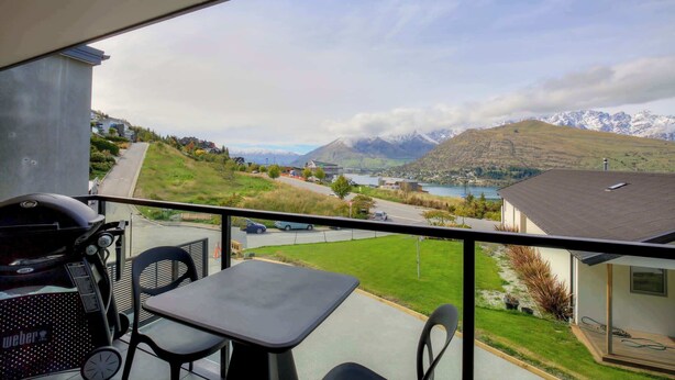 A balcony with a grill, table, and chairs, overlooking a mountainous landscape with a lake and buildings. - Remarkable Lake View (Queenstown)