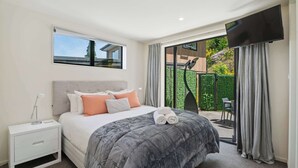 A bedroom with a bed, nightstand, TV, and a view of a garden. - Remarkable Lake View (Queenstown)