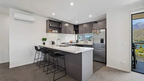 A modern kitchen with a central island, bar stools, a refrigerator, and a view of a mountainous landscape. - Remarkable Lake View (Queenstown)