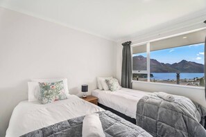 Hotelkamer met twee bedden, een nachtkastje, een lamp en een groot raam met uitzicht op een berg en meer.