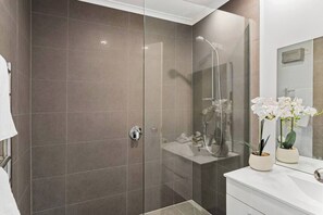 Een moderne badkamer met een douchecabine van glas, een witte wastafel en twee orchideeën in potten op het aanrecht.