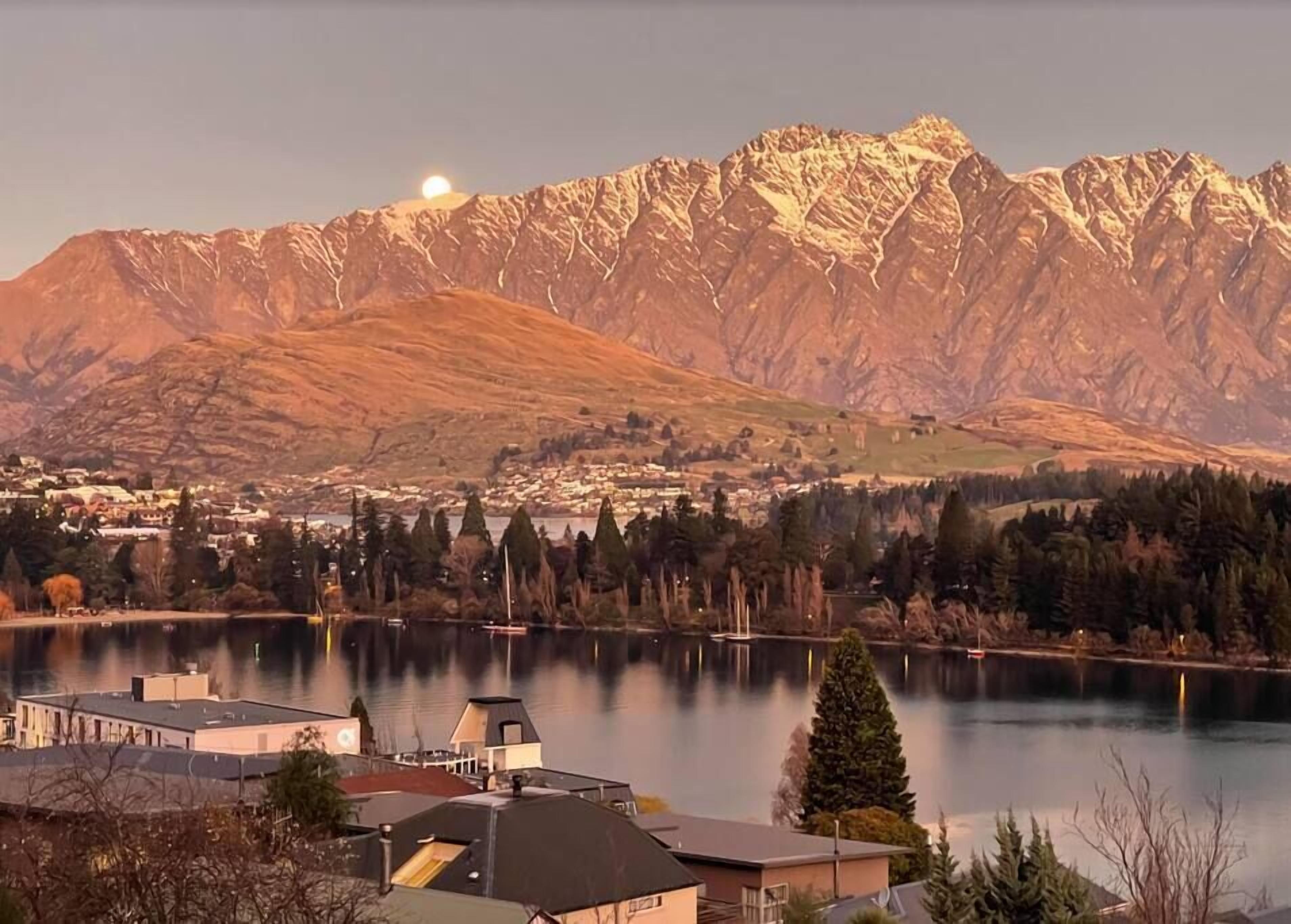 A lakeside view with mountains in the background, buildings along the shore, and a clear sky.