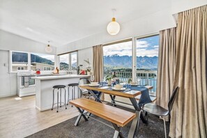 Une cuisine moderne dotée d’un îlot central, de tabourets de bar et d’une table à manger avec des chaises. Une grande fenêtre offre une vue sur les montagnes et un lac.
