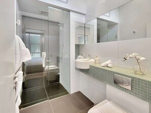 A modern bathroom with a glass shower enclosure, a white sink, and a glass vase with flowers on the countertop. - Lake Views & a quick walk to town! (Queenstown)