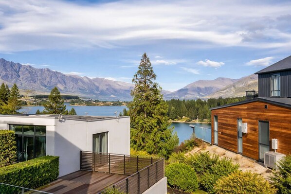 A modern house with a wooden deck, a view of a lake, and mountains in the background.