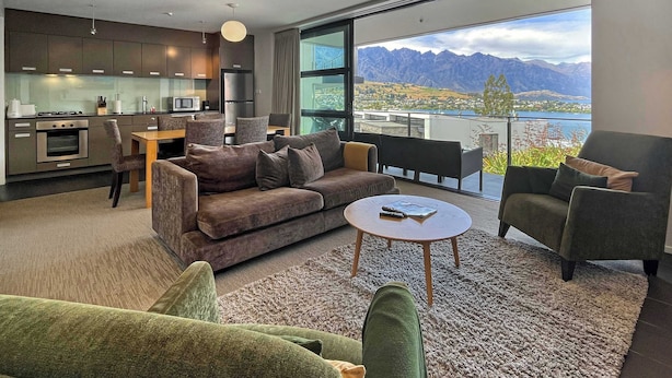 Ein modernes Wohnzimmer mit einer Couch, Sesseln, einem Couchtisch und Blick auf Berge durch große Fenster.