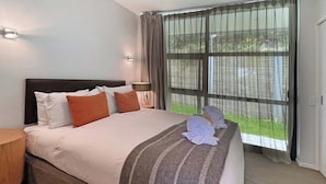 Ein Hotelzimmer mit einem großen Bett, einem Nachttisch, einer Lampe und einem Fenster mit Vorhängen.