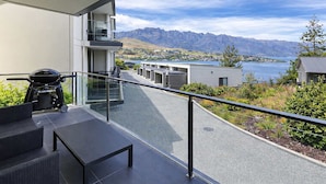 Ein Balkon mit Grill, Tisch und Stühlen mit Blick auf eine Berglandschaft und ein Gewässer.