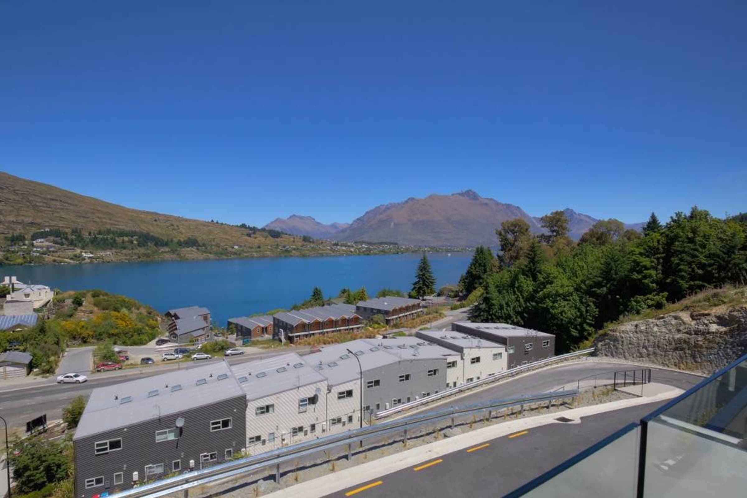 Vista de un pueblo a orillas del lago, con edificios, una carretera y montañas al fondo.