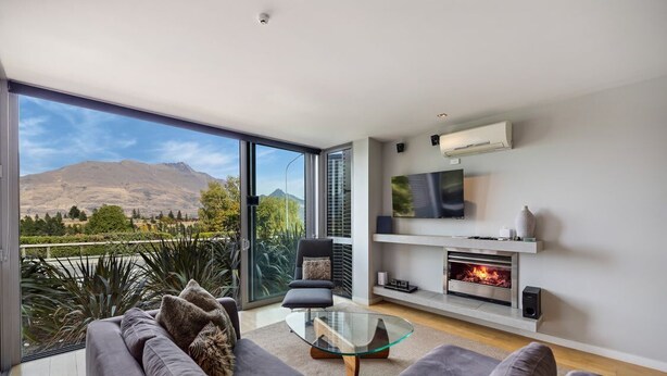 Een moderne woonkamer met een grote glazen deur die uitkomt op een balkon, een open haard, een televisie en een comfortabele zithoek.