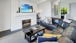 Una sala moderna con chimenea, televisor de pantalla plana, sofá de cuero y una mesa de centro.