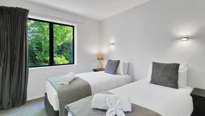 Habitación de hotel con dos camas, una ventana con cortinas, una mesita de noche con lámpara y vistas al exterior.