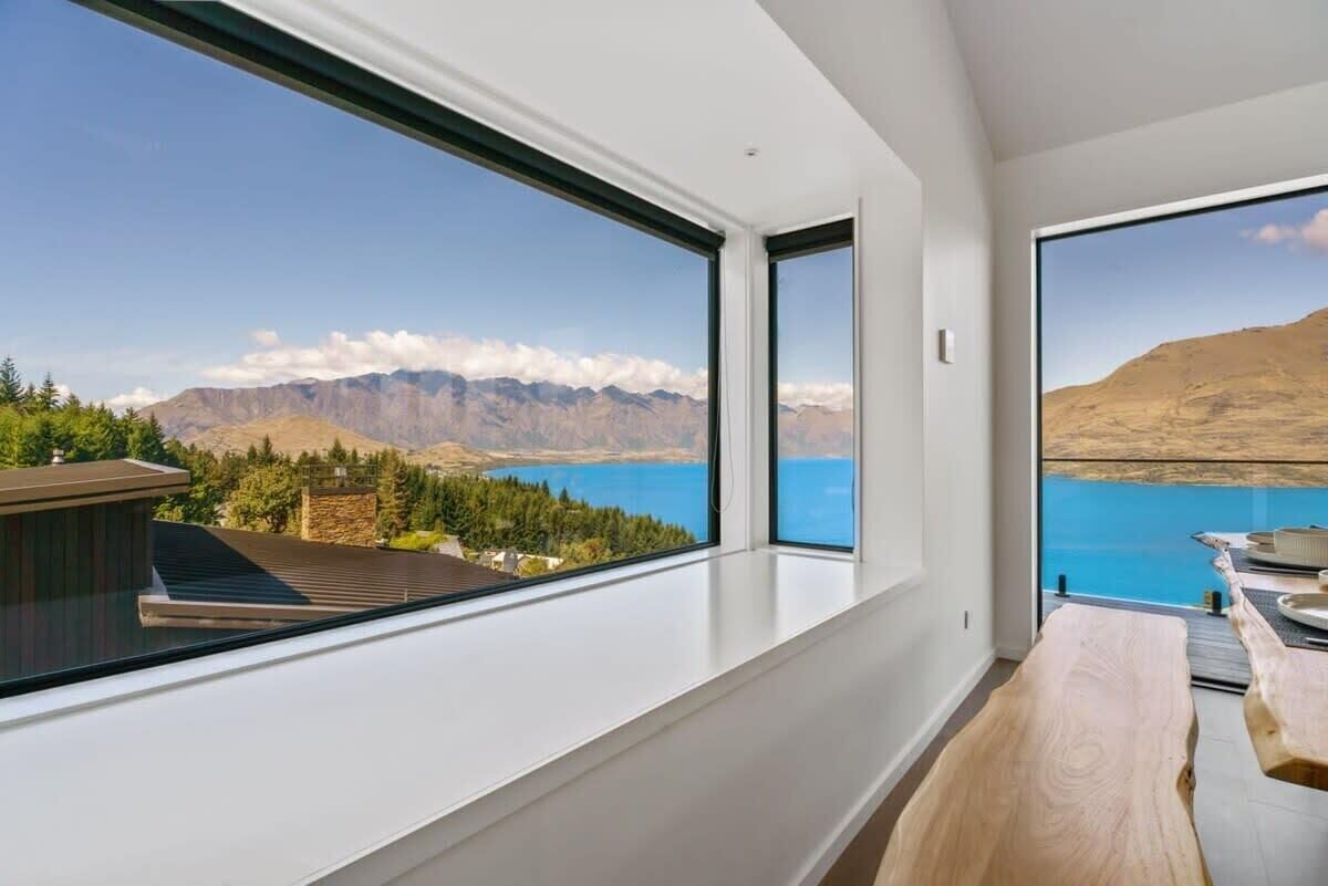 A modern room with large windows offering a view of mountains and a lake. - Lakeview Paradise On Wynyard (Queenstown)