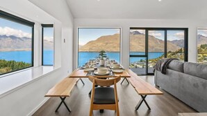A modern dining area with a wooden table set for four, large windows offering a view of mountains and a lake. - Lakeview Paradise On Wynyard (Queenstown)