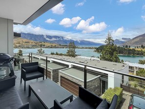 Un balcon avec vue sur un lac et des montagnes. Il y a des espaces de détente en plein air avec des tables et des chaises.