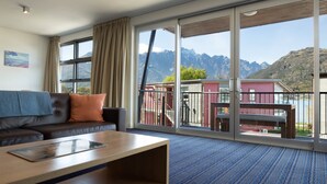Une chambre d’hôtel moderne dotée d’une grande porte-fenêtre coulissante donnant sur un balcon avec vue sur les montagnes.